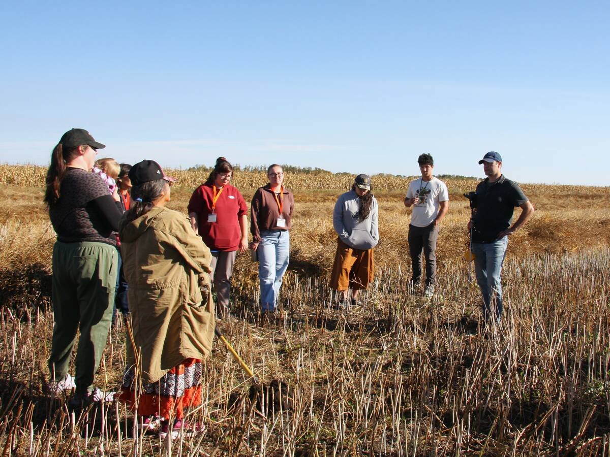 Attendees of the Indigenous Farm and Food Festival in Batoche, Sask., co-hosted by the Bridge to Land Water Sky Living Lab stand in a swathed canola field in late September 2025. The event highlighted several practices and concepts that fit under the umbrella of regenerative agriculture. Photo: Janelle Rudolph