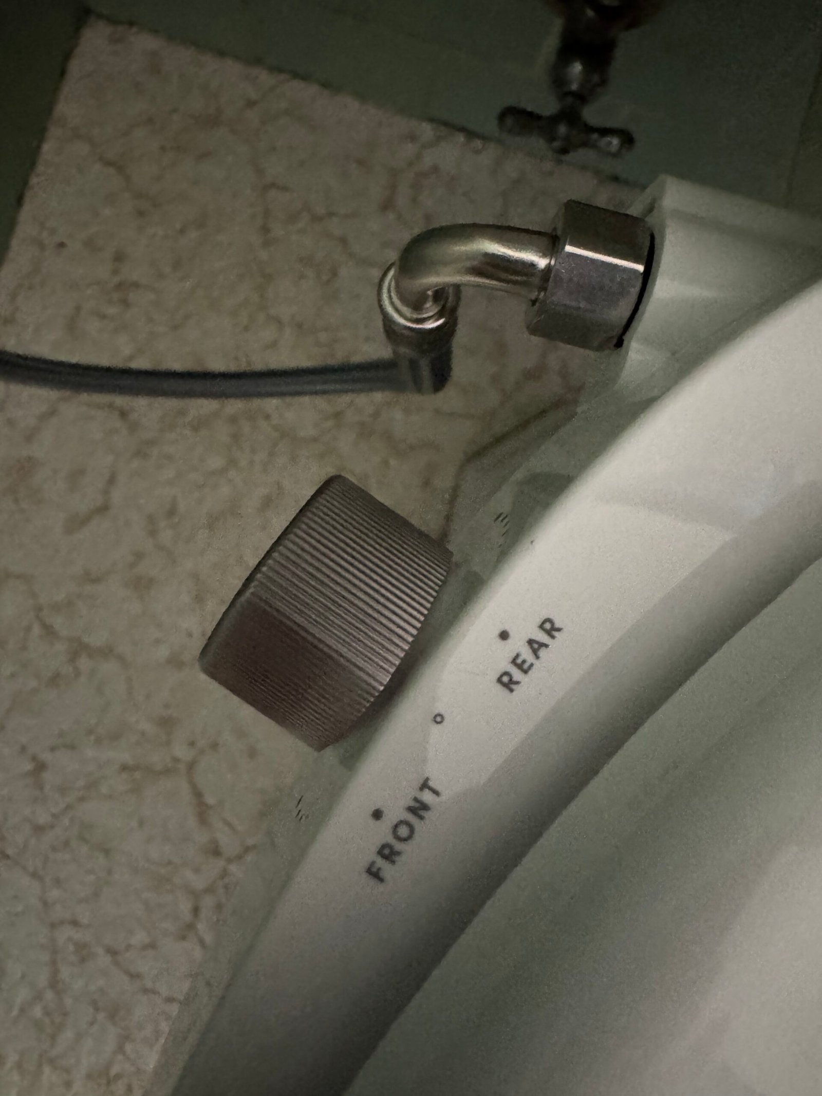 A close-up of a control knob labeled “Front” and “Rear” on a white appliance, with a metal hose connected above it.