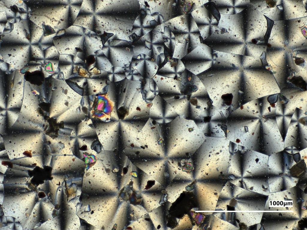 A microscopic view of the kaleidoscope-like crystal structures of two NASA-made material samples, a gray sample on the left and a reddish sample on the right.