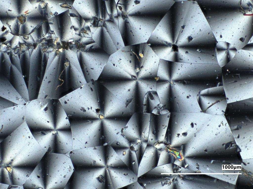 A microscopic view of the kaleidoscope-like crystal structures of two NASA-made material samples, a gray sample on the left and a reddish sample on the right.