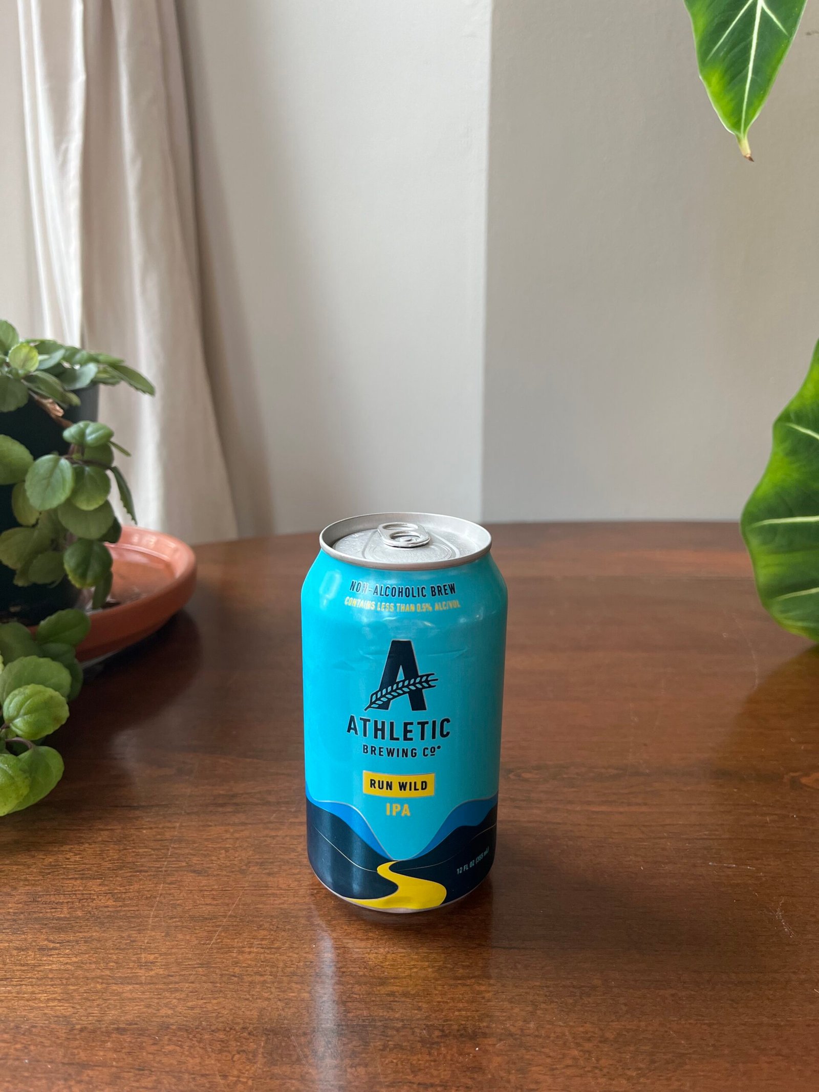 A can of Athletic Brewing Co. Run Wild IPA non-alcoholic beer sits on a wooden table next to a plant.