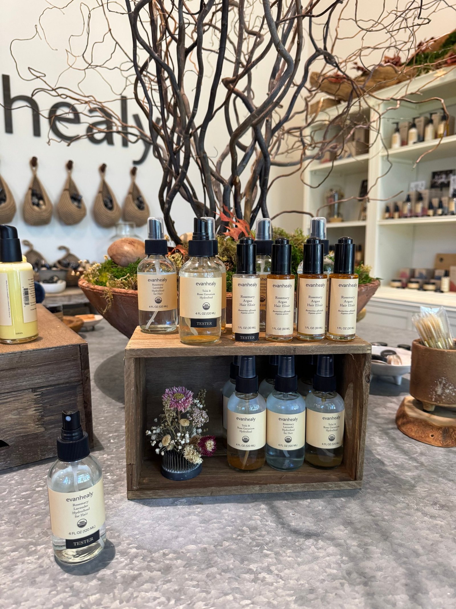Assorted evanhealy hair care products, including glass spray bottles and dropper bottles, displayed on wooden shelves and a counter.