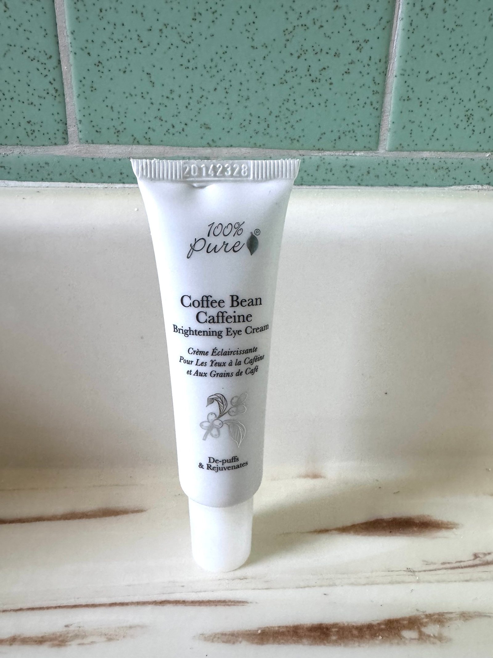 A white tube of 100% Pure Coffee Bean Caffeine Brightening Eye Cream standing on a bathroom counter.