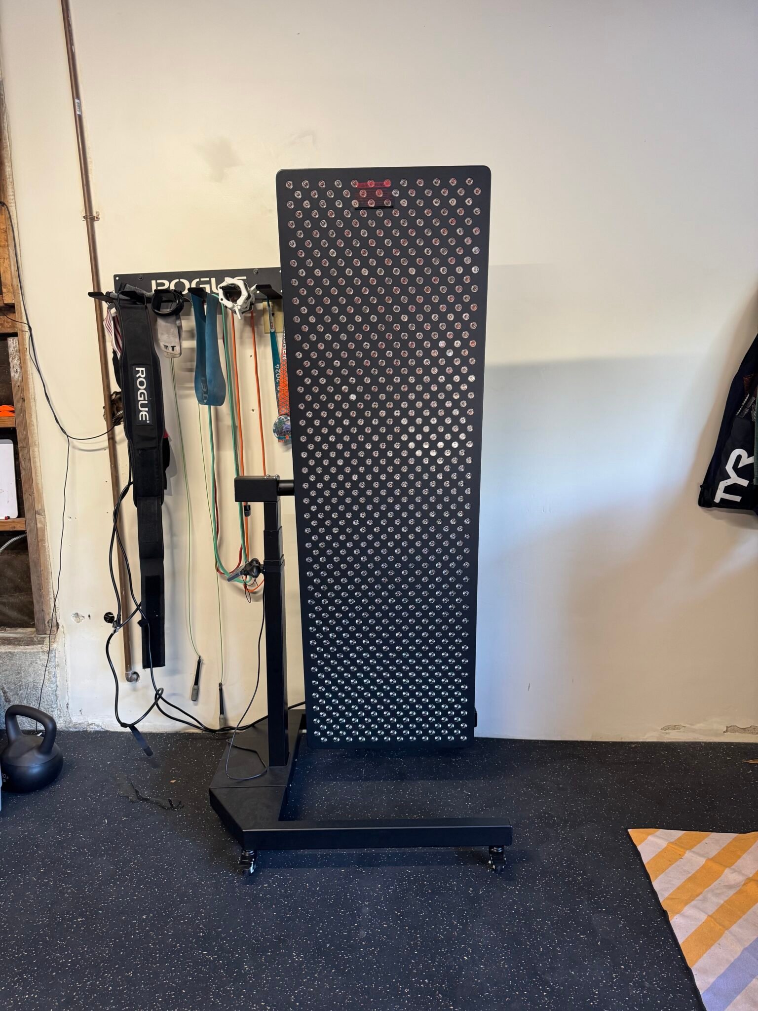 A Reflexion training board with a dotted pattern stands in a home gym, next to resistance bands, a kettlebell, and other workout equipment.
