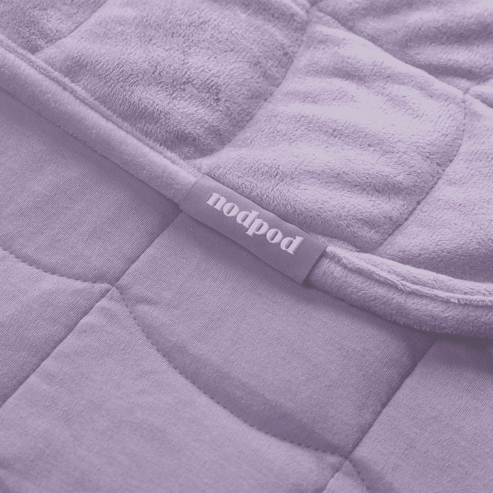 Close-up of a quilted fabric product with a visible “nodpod” label attached to the seam. The image has a purple color filter.