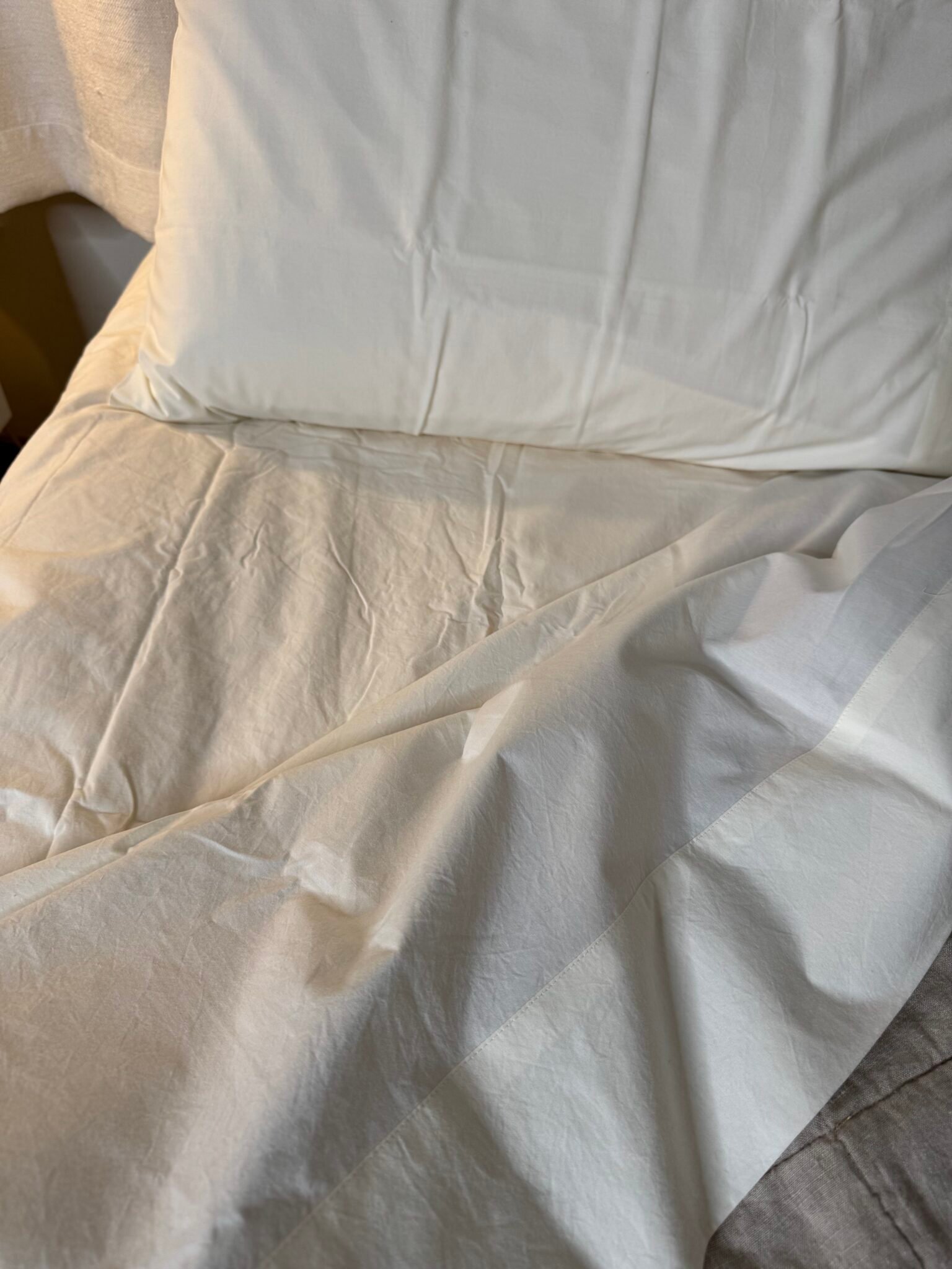 A close-up view of a neatly made bed with white sheets and a pillow.
