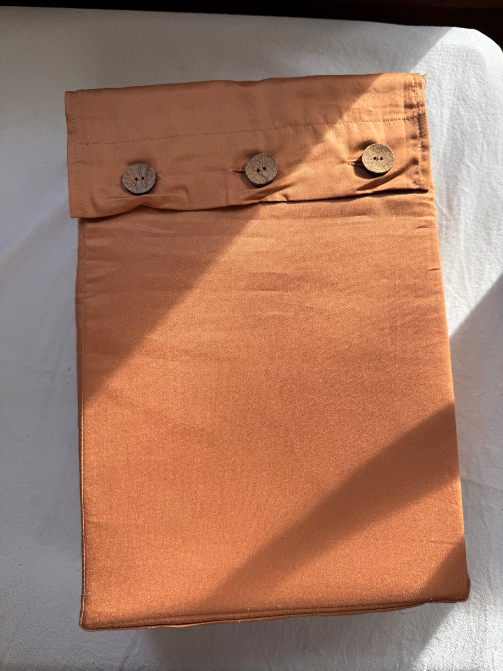 A folded, peach-colored fabric bag with three wooden buttons lying on a white surface.