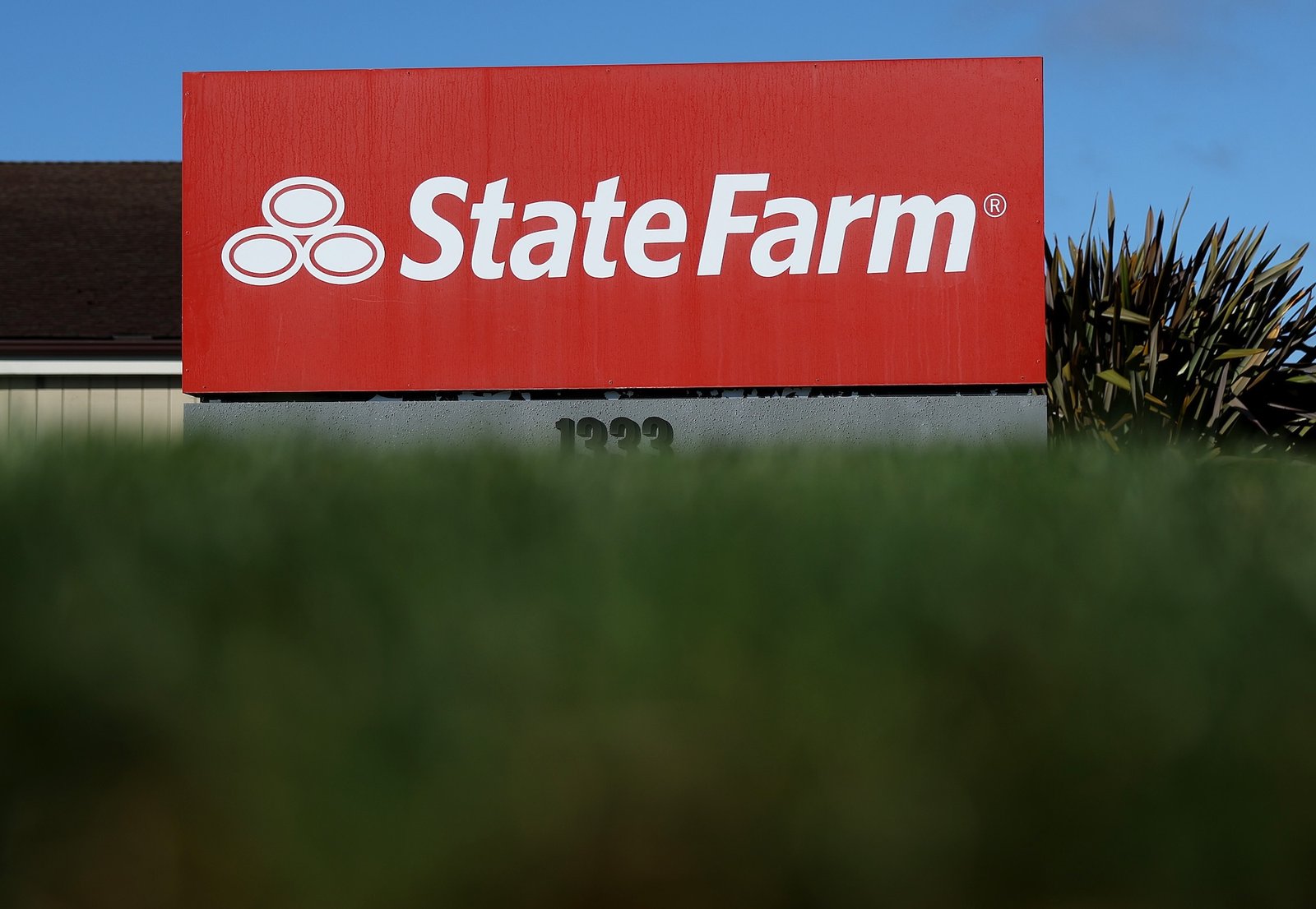 a sign for a state farm insurance branch partially covered by a green hedge