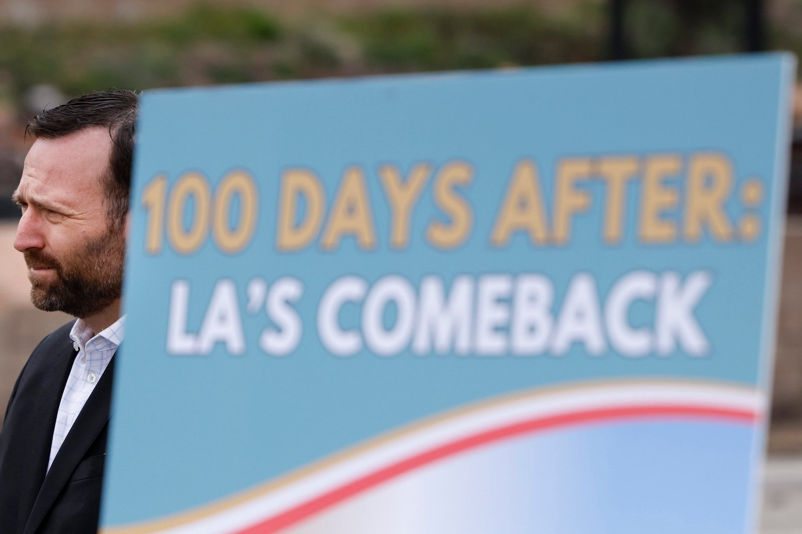 A man in a suit stands near a sign that says '100 days after: LA comeback'