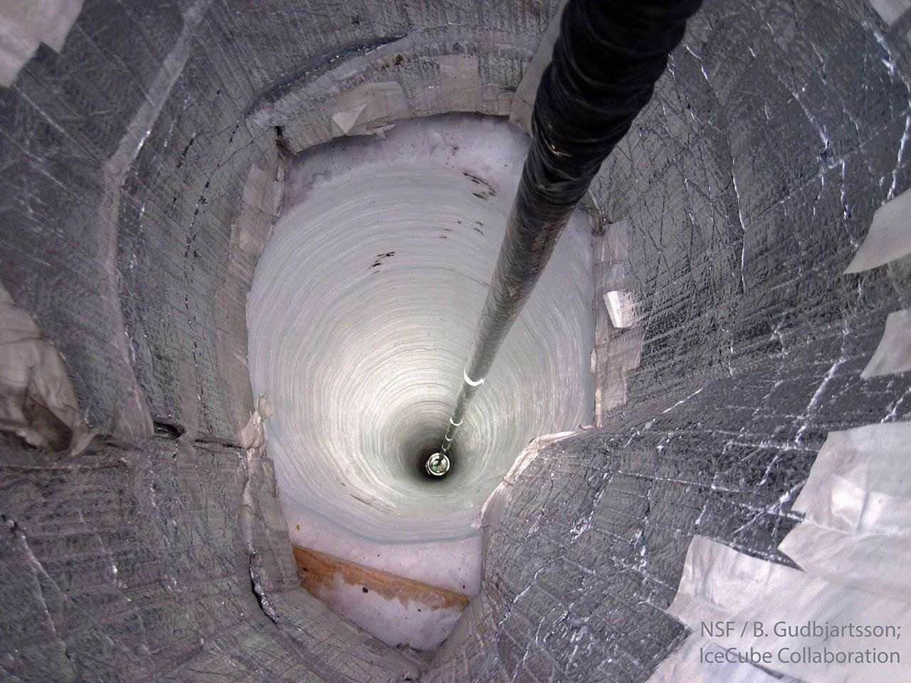 A dark cable descends into a deep carved hole of ice. The hole is so deep that it disappears into darkness. Please see the explanation for more detailed information.
