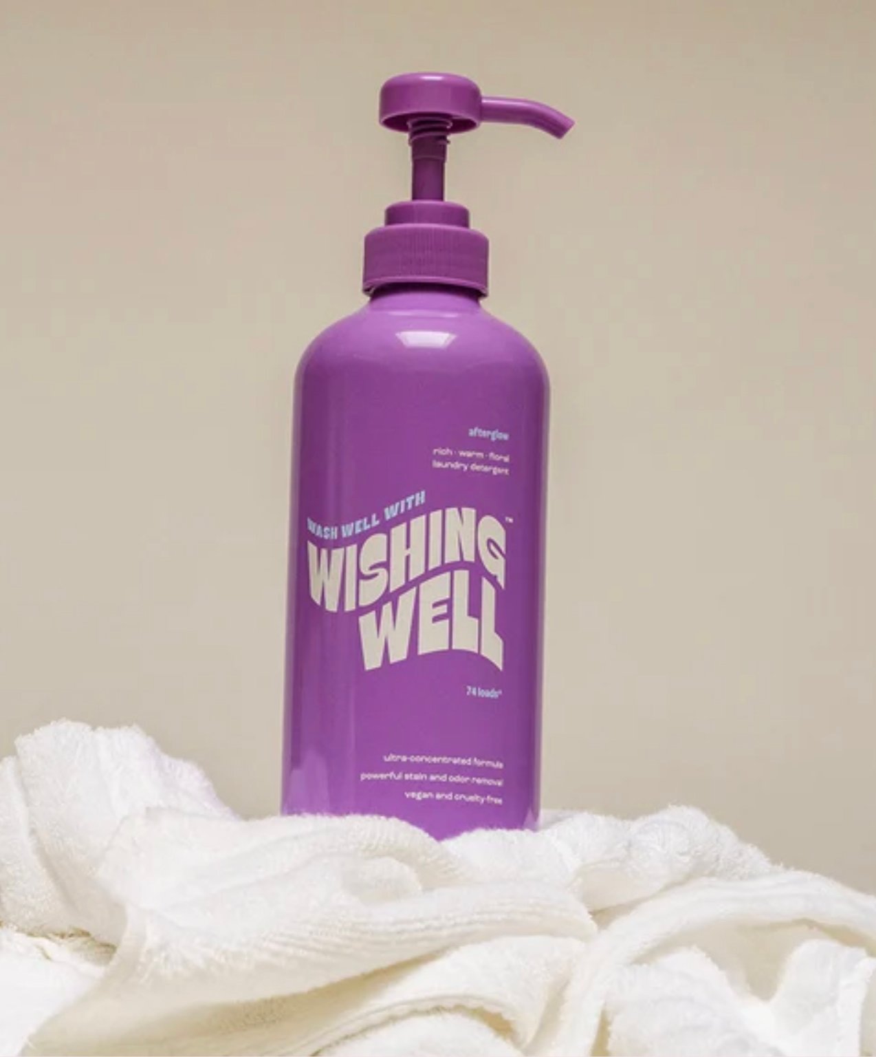 A purple pump bottle labeled “Wishing Well” sits on white towels against a neutral background.