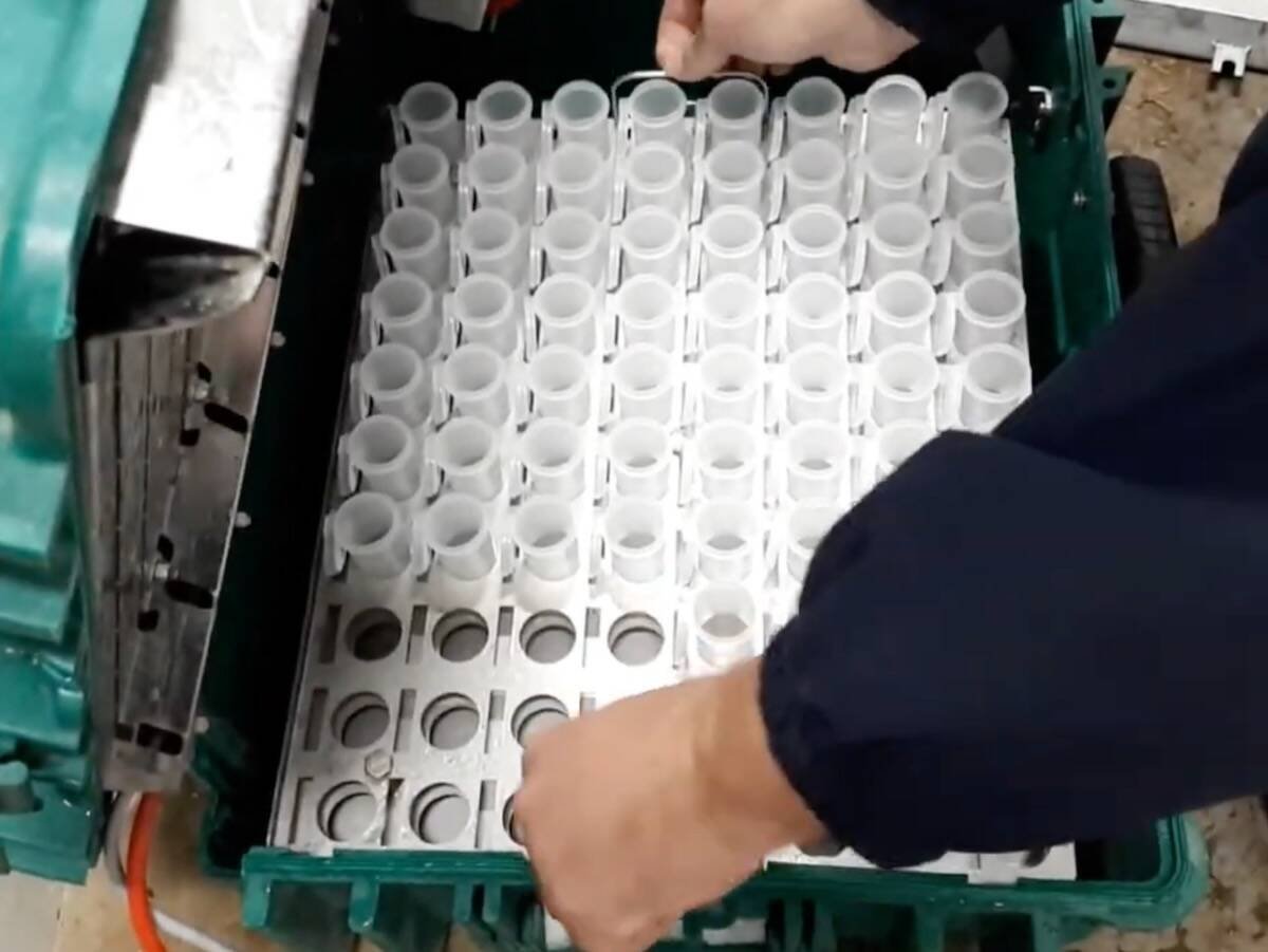 Hands loading empty milk sample vials into a tray beside teal robotic milking equipment. Photo: Lactanet Canada video screengrab via YouTube