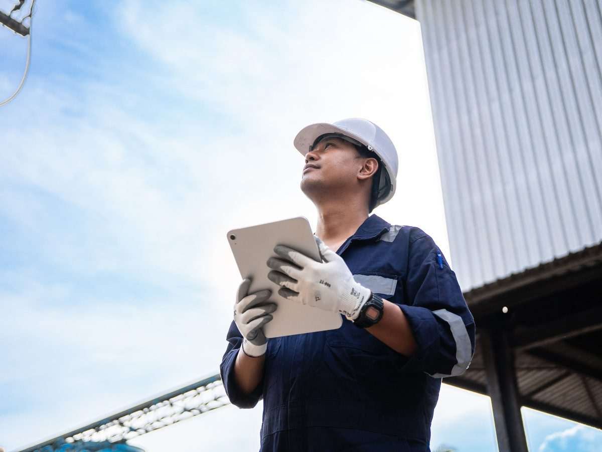 Engineer with clipboard or tablet looks upwards as though inspecting elevated equipment or chimney