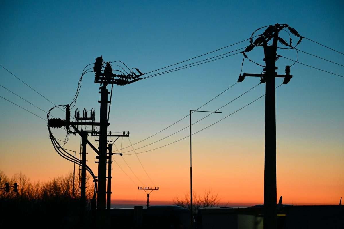 Silhouettes of electricity distribution poles, insulators and overhead power lines against a blue and orange sunset sky