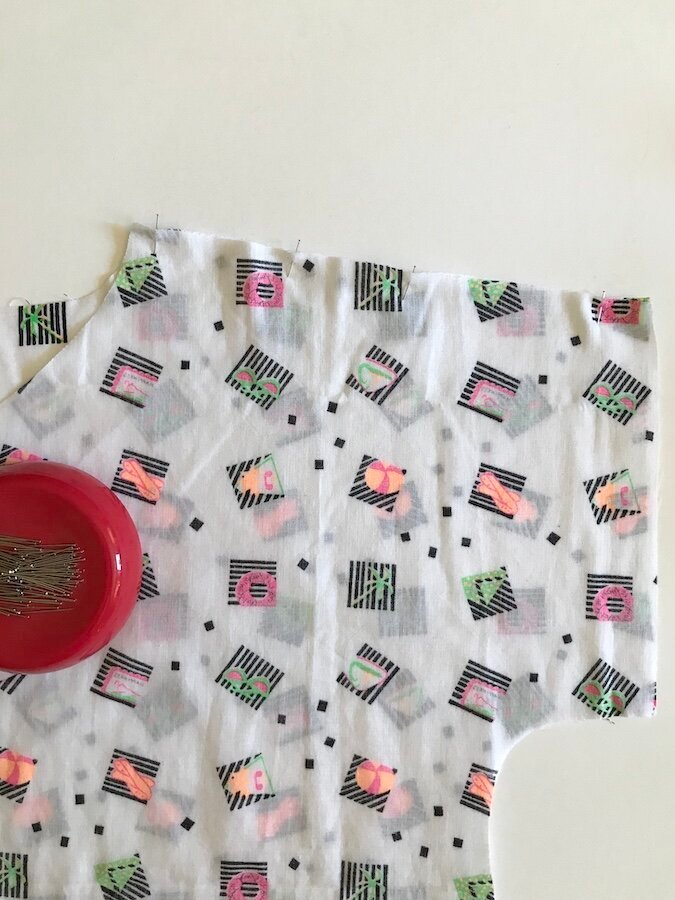 A piece of white patterned fabric with pins in it.