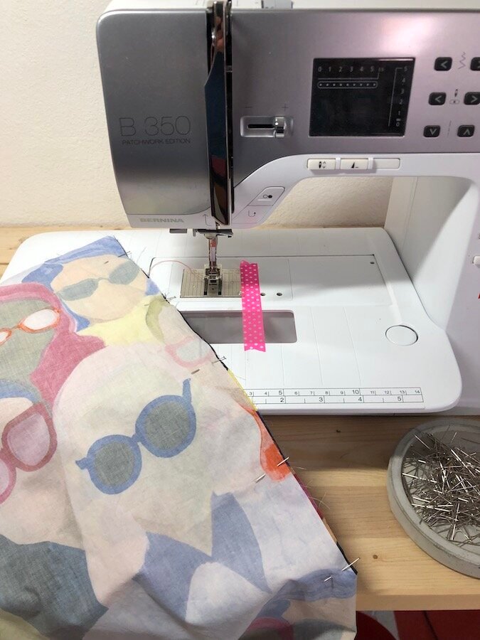 A piece of fabric with pins in it, being sewn on a sewing machine.