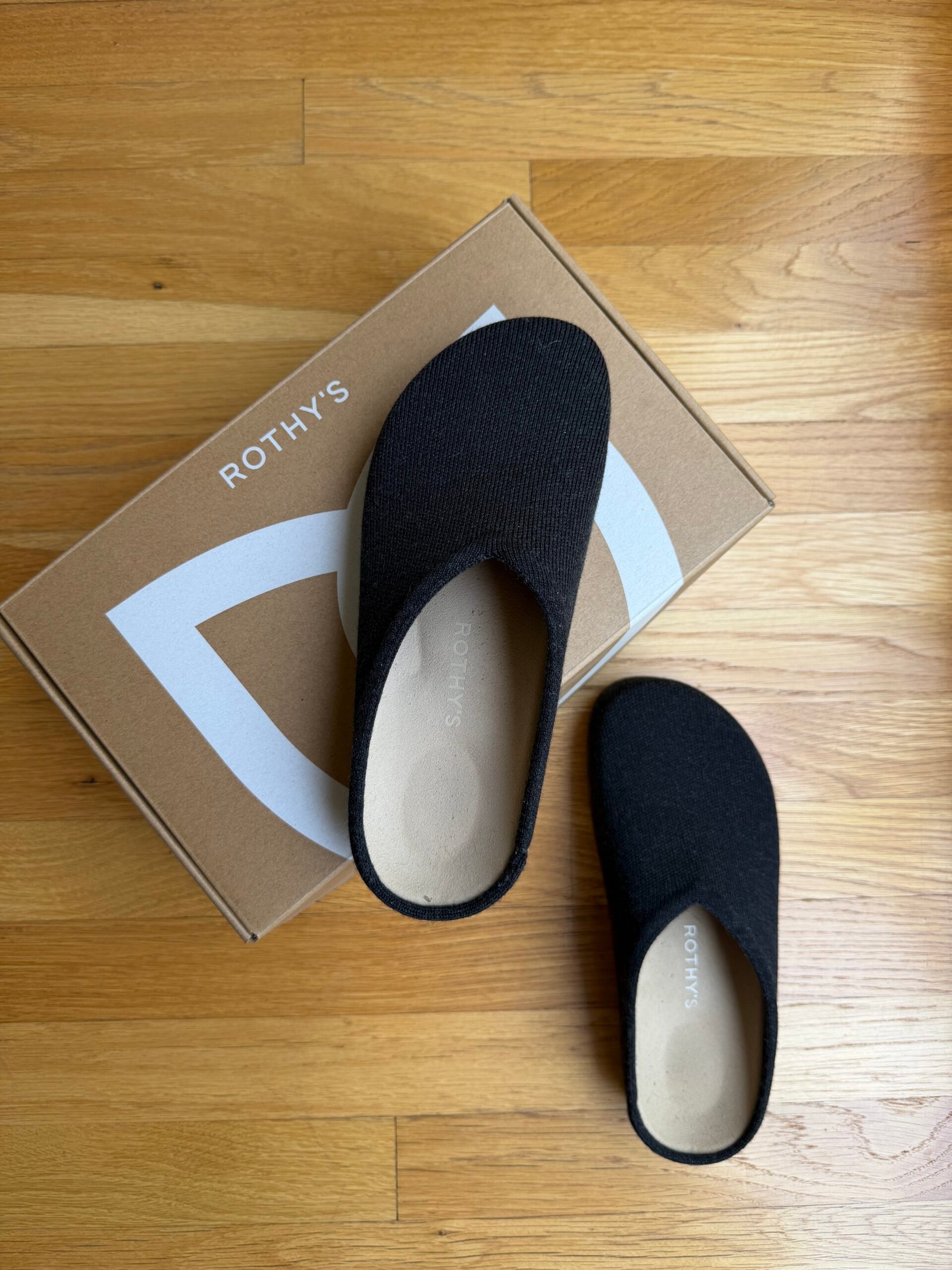 A pair of black Rothy’s slip-on shoes resting on top of a Rothy’s branded cardboard box.