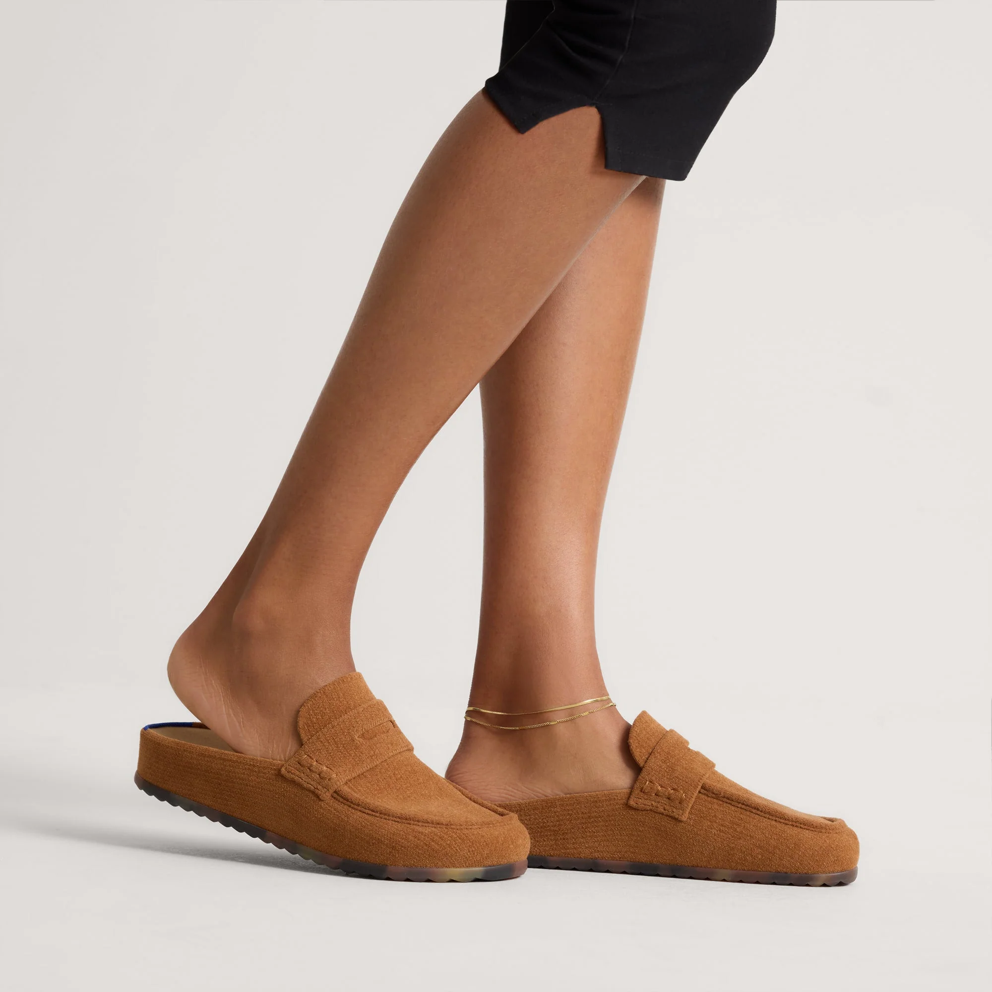 A person wearing tan slip-on loafers with a textured finish.