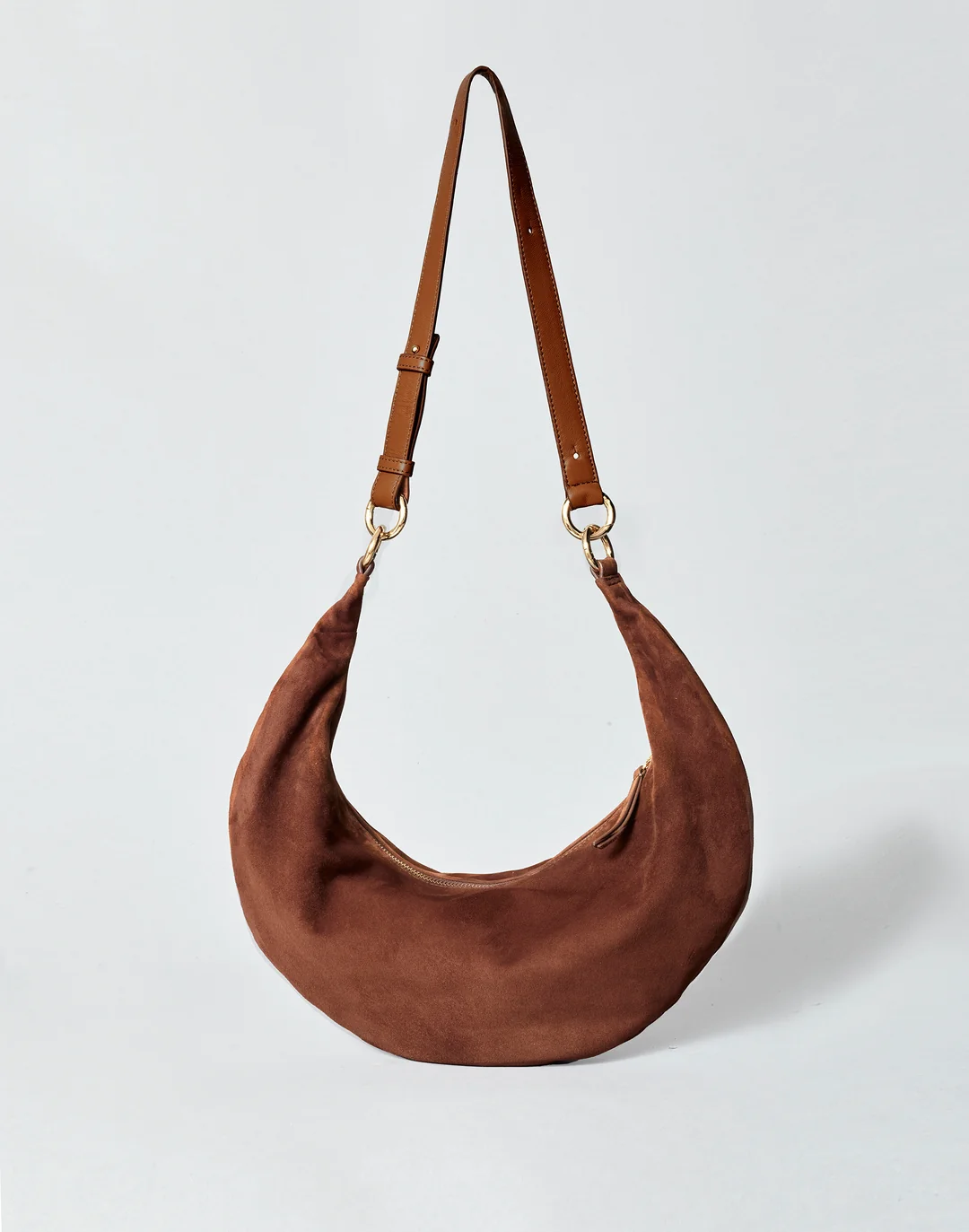 A crescent-shaped brown suede shoulder bag with a thin leather strap and gold-tone hardware.