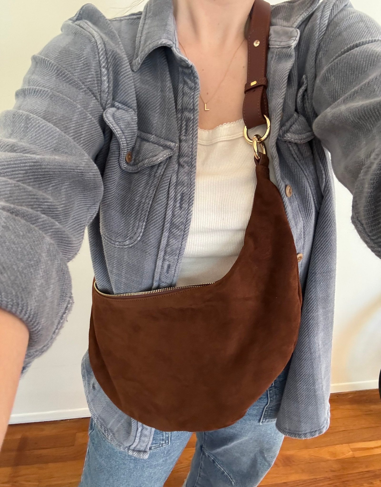A person wearing a blue button-down shirt over a white top, carrying a brown crescent-shaped shoulder bag.