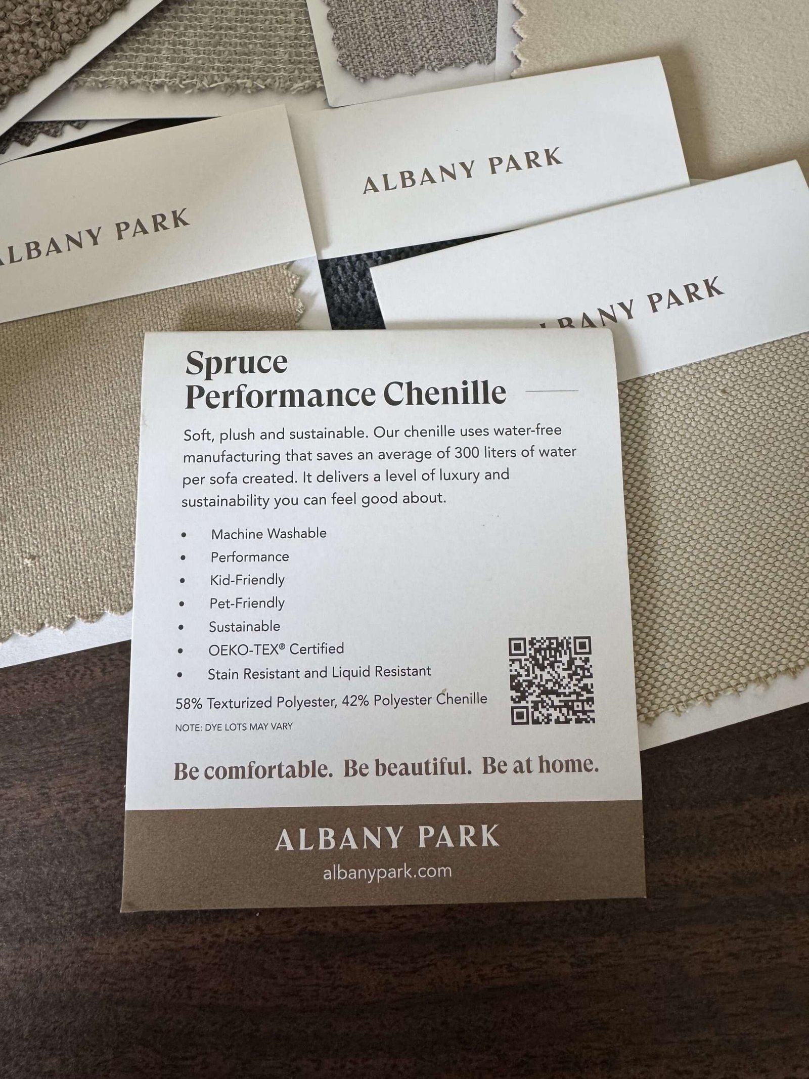 A card describes "Spruce Performance Chenille" fabric by Albany Park, listing features like machine washable, pet-friendly, and sustainable, with fabric swatches and business cards nearby.