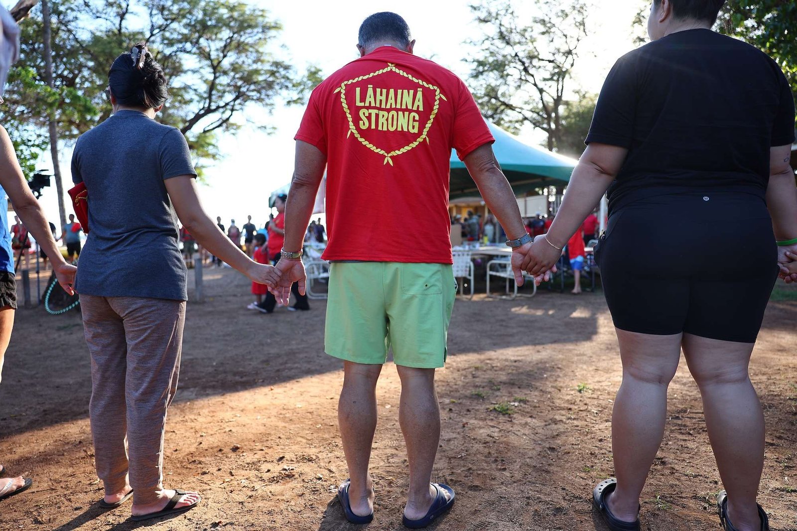 People hold hands during a prayer circle wearing a shirt that says Lahaina strong