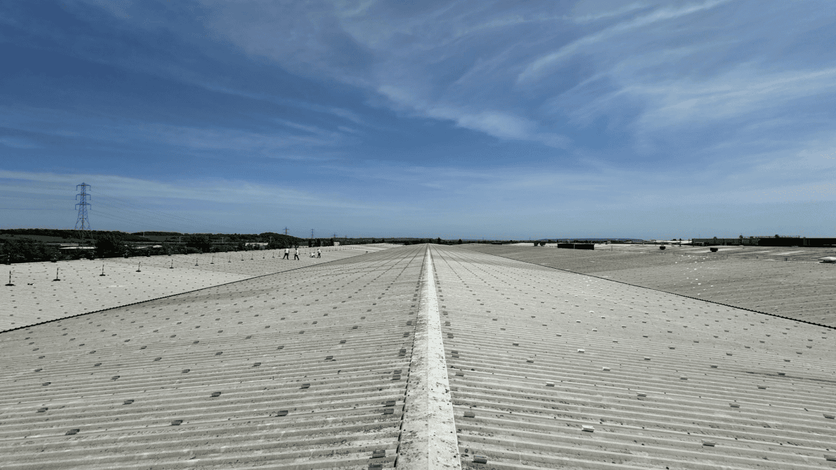 View along the vast roof of Refresco's Bridgwater factory, showing rows of solar panel mounting fixtures and workers in high-visibility clothing.