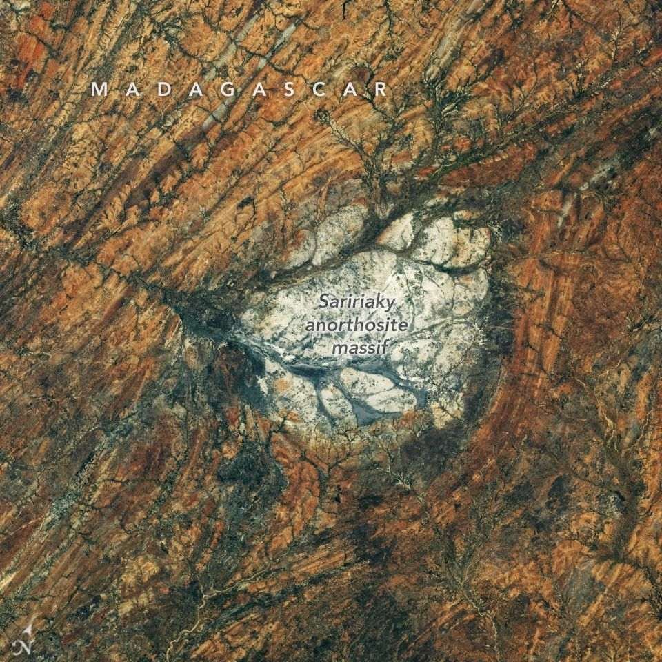 A round, white rock outcrop is surrounded by orange rocks with a north-south linear pattern. Branching riverbeds cut through the rock structures.