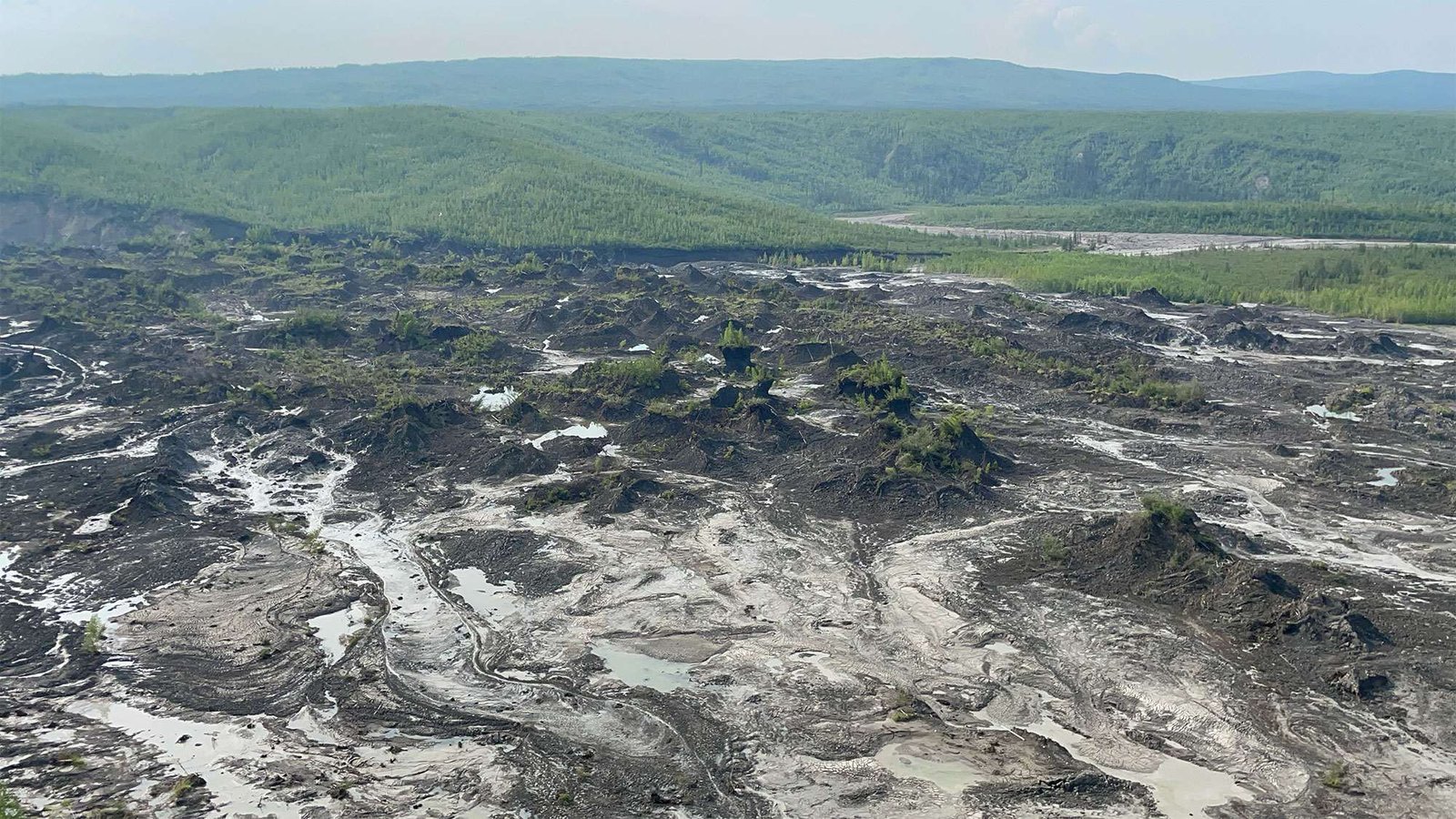 landscape showing damaged earth caused by permafrost detachment slides with tree covered hills in the background