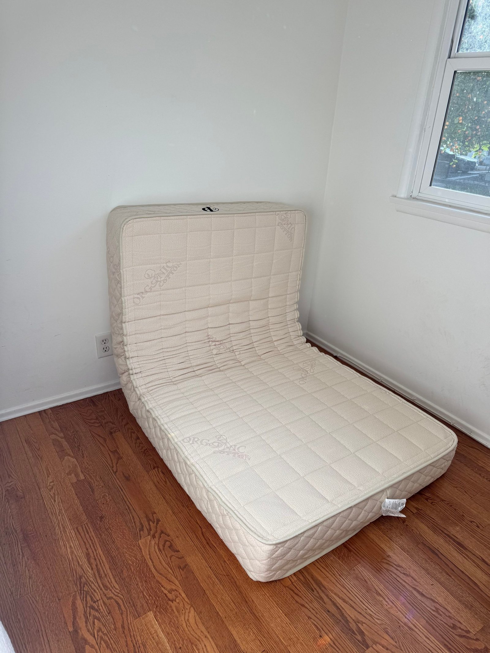 An organic cotton mattress folded in half against a white wall on a wooden floor.