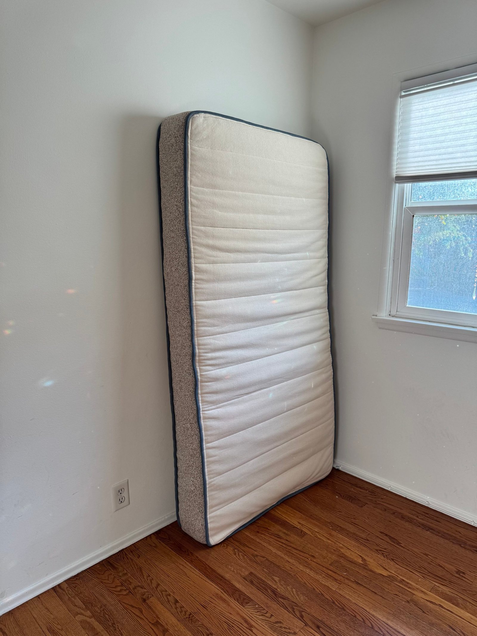 A single mattress propped upright against a corner wall in an empty room.