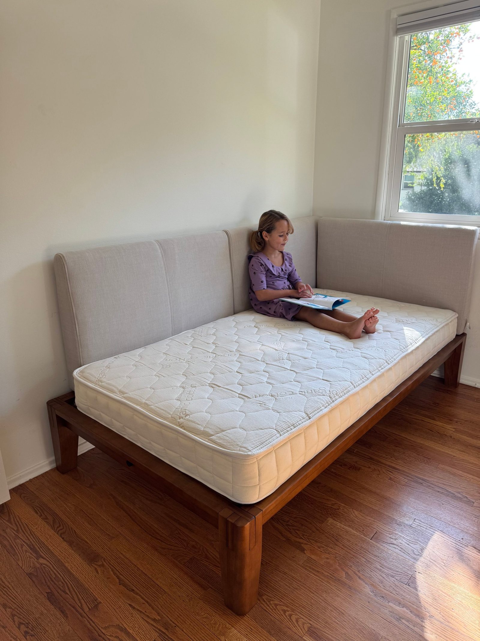 A young girl sits on a corner daybed reading a book.