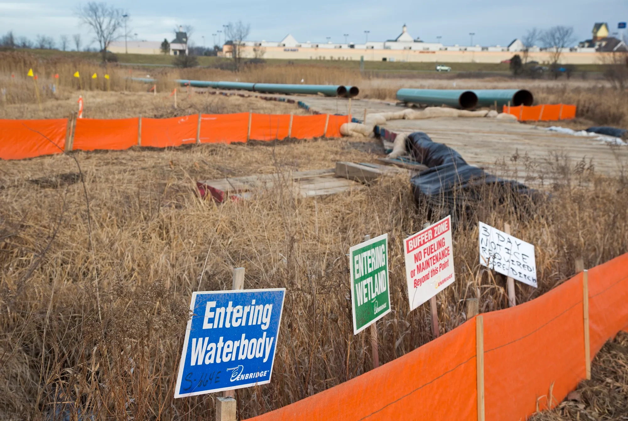 pipeline signs and orange construction fences surround parts of a midwestern wetland