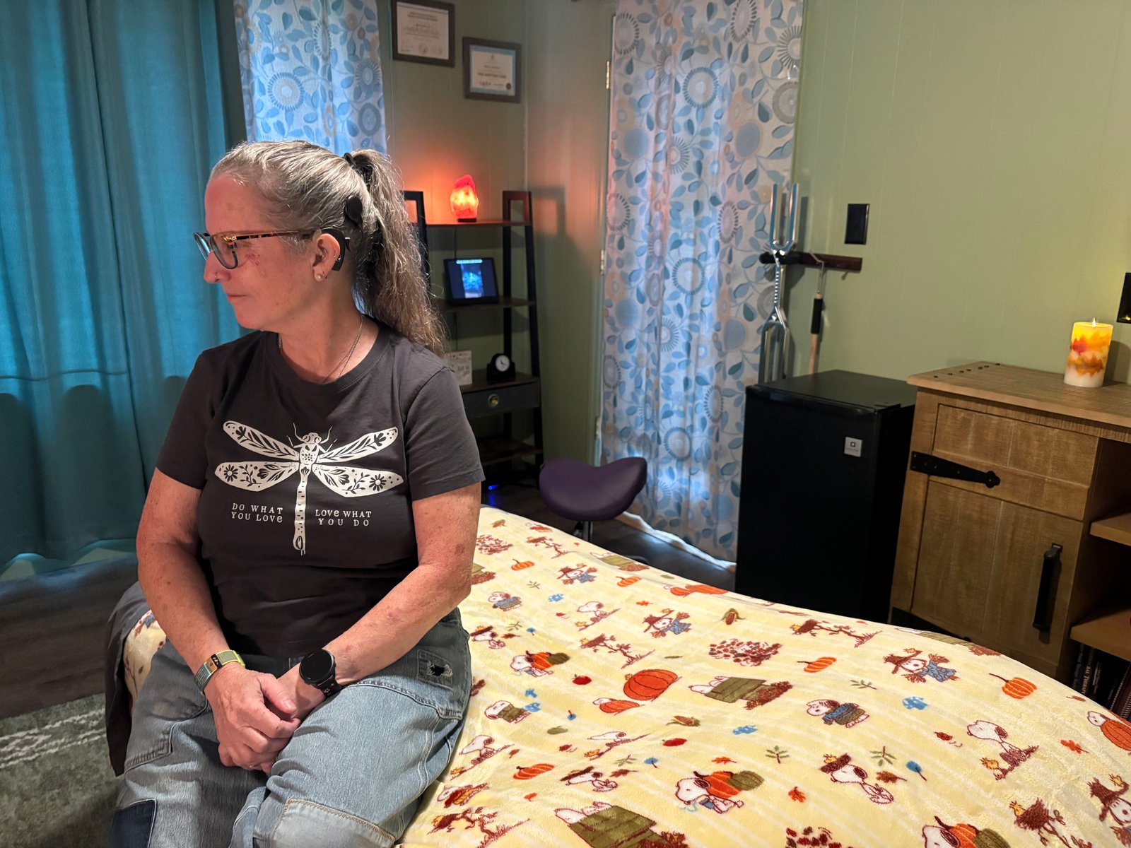 A woman with a cochlear implant sits on a bed