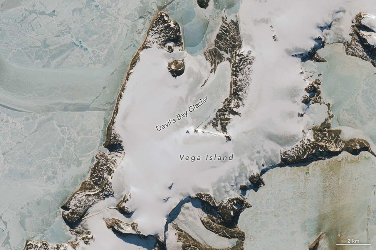 Part of an ice-covered Antarctic island has the appearance of a grinning skull in profile. Some of the face has a gray appearance where seasonal snow is gone and bare ice is exposed.