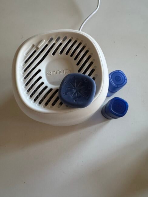 A white Canopy diffuser with a blue disk on top and two blue essential oil bottles beside it, placed on a white surface.