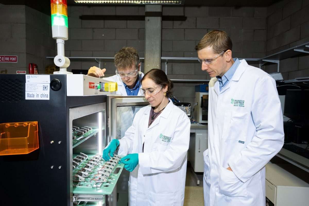 Three researchers in laboratory coats and safety glasses examine samples and equipment in a University of Limerick laboratory