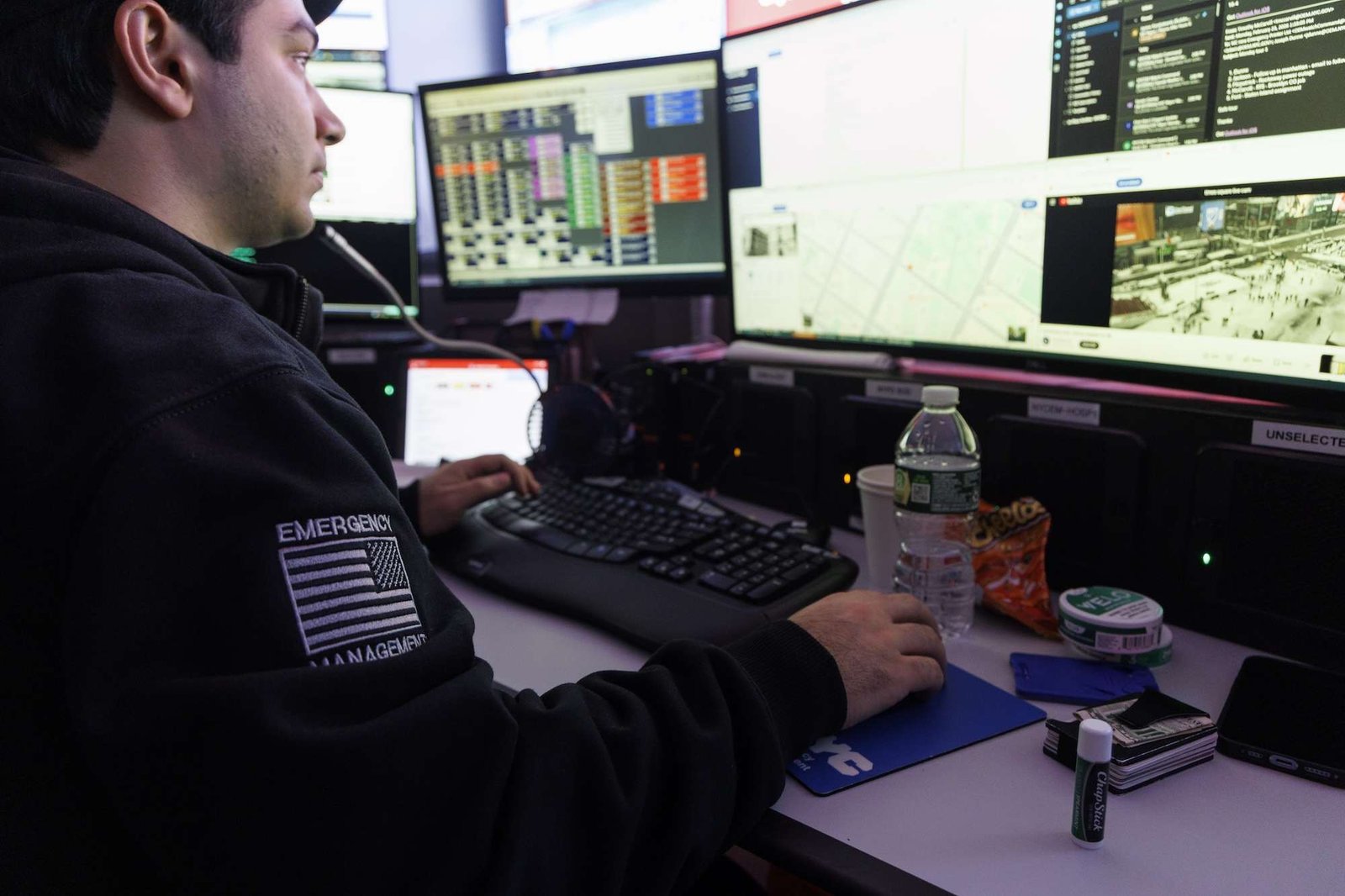 a man in an emergency manager uniform monitors several screens showing weather data